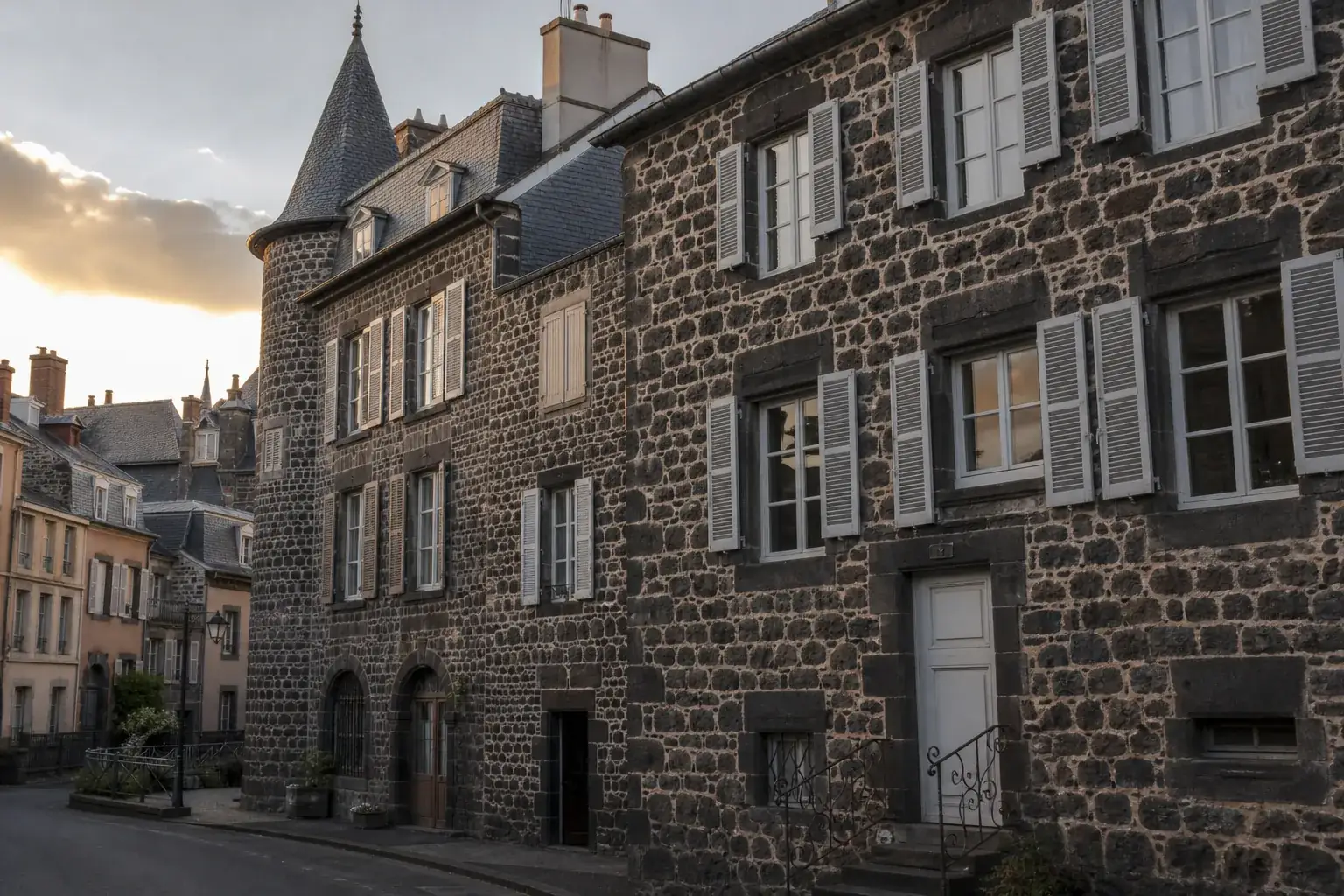 Vue urbaine discrète d’une architecture typique d’Auvergne en pierre volcanique noire, lumière de fin de journée